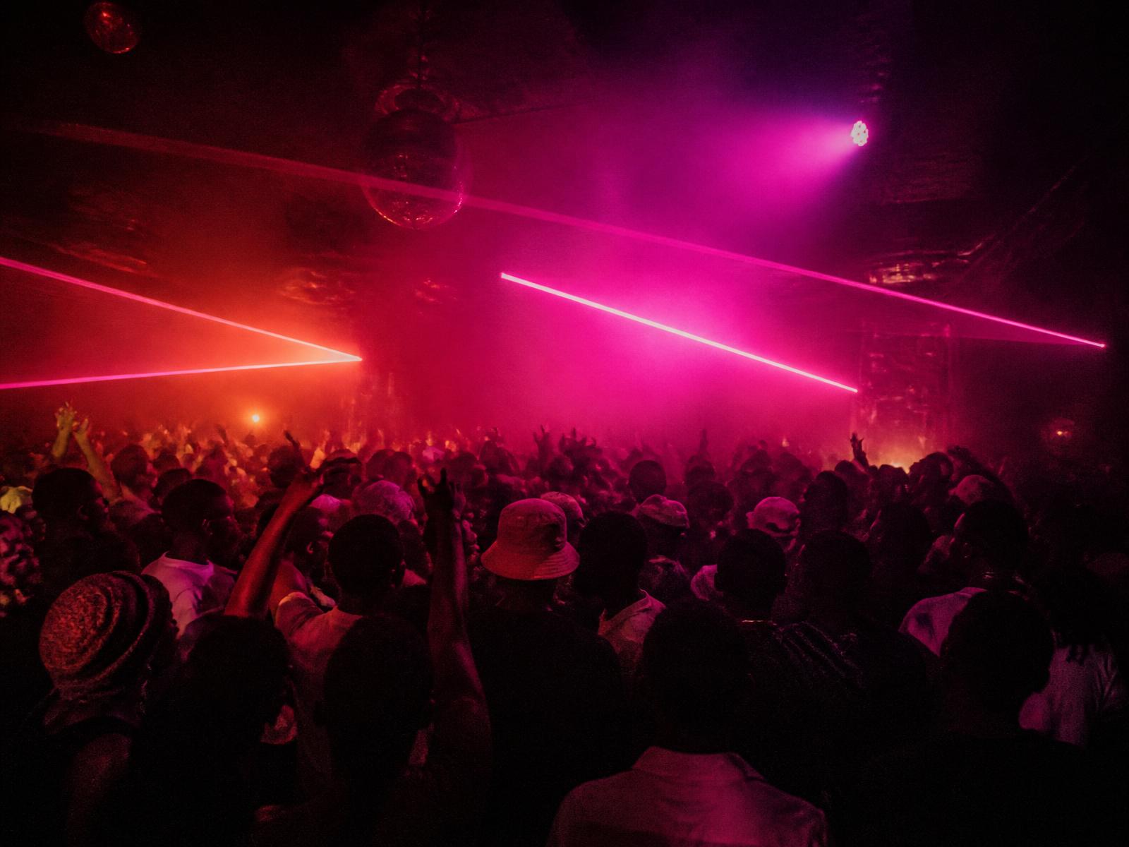 A packed amapiano dance floor lit by pink and coral lasers